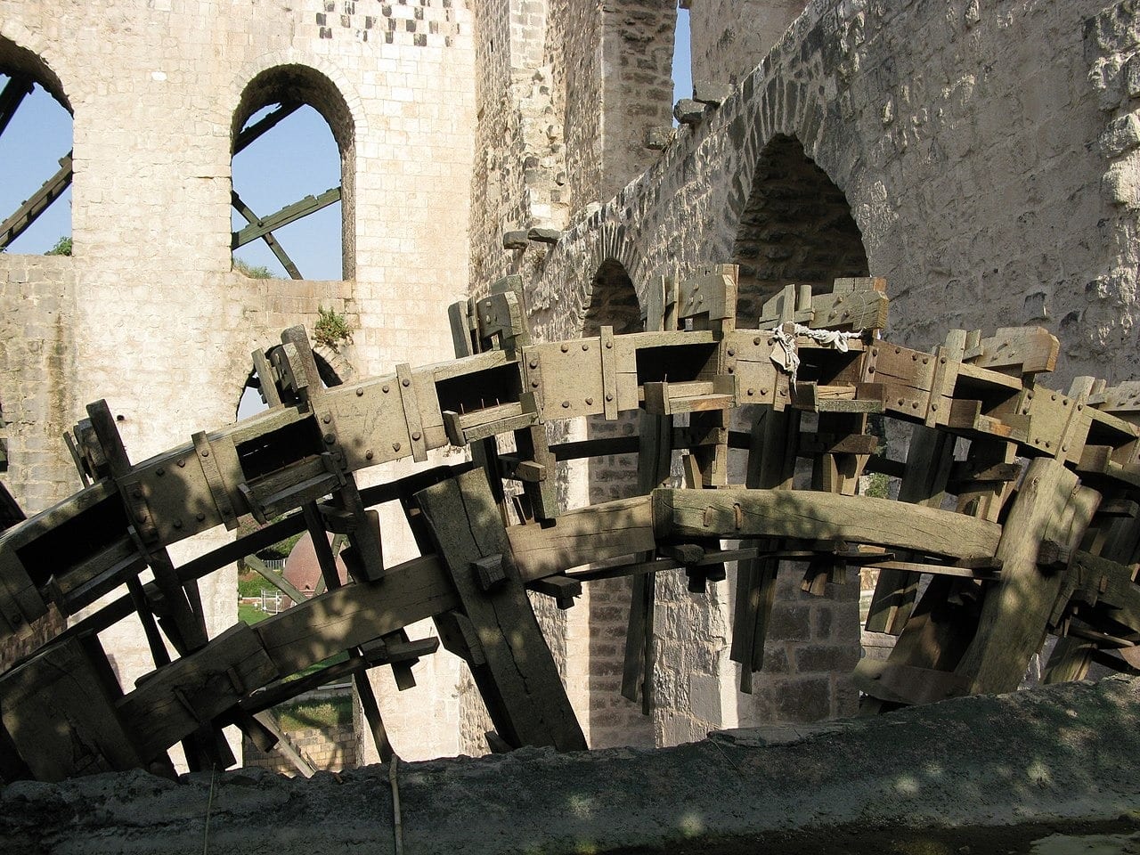 Noria al-Muhammadiyya. On rim of wheel are wooden water-collection boxes with large openings and spouts. In foreground is top edge of the stone aqueduct into which they pour.