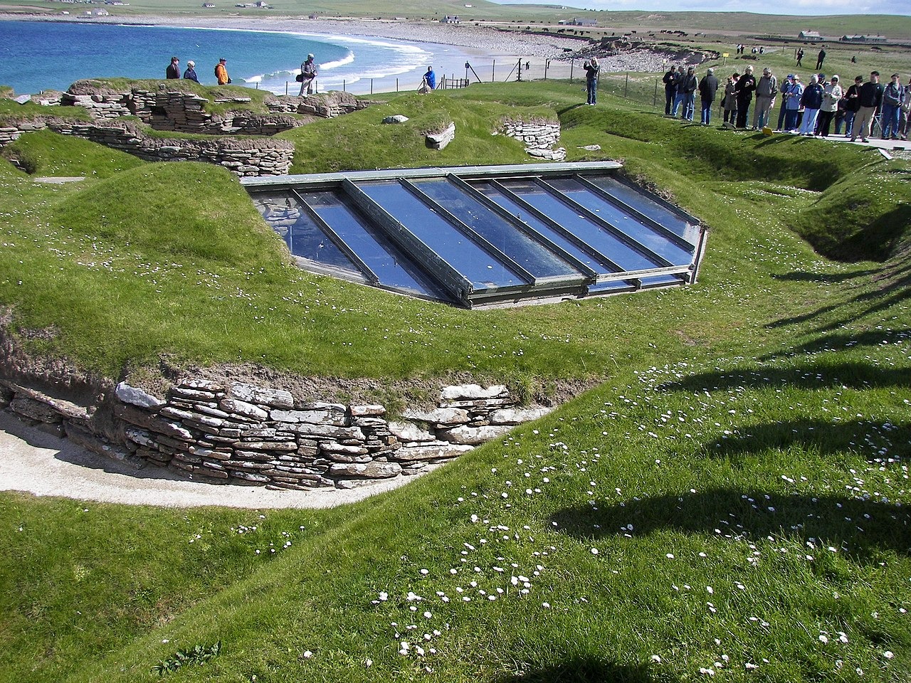 View over the settlement, showing covering to house No. 7 and proximity to modern shore line. The glass roof has now been replaced by a turf one, as the humidity and heat caused by the glass roof were hindering preservation